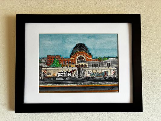 Framed artwork of a cityscape with a prominent building on a beige wall.