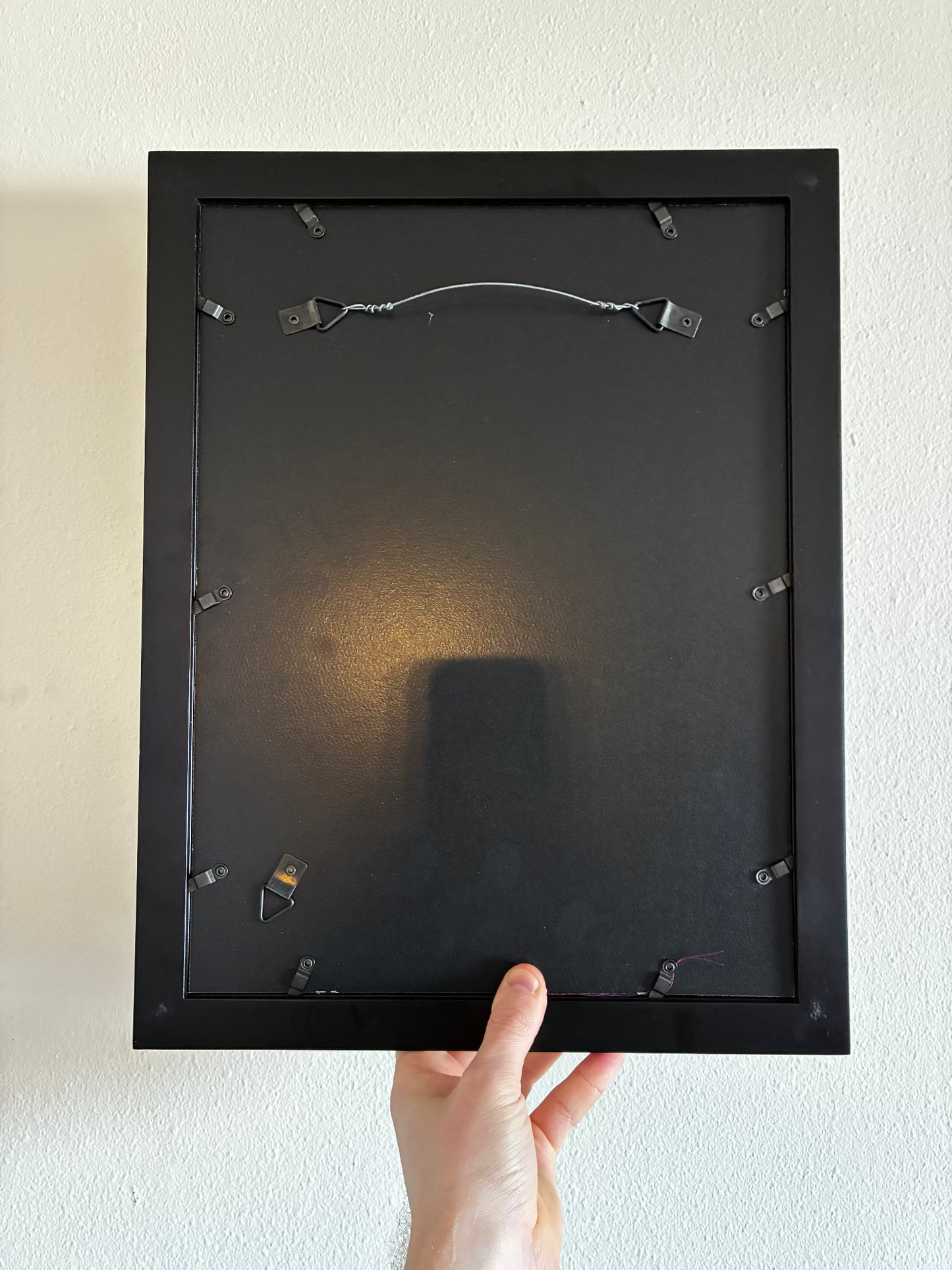 Black picture frame held against a white wall
