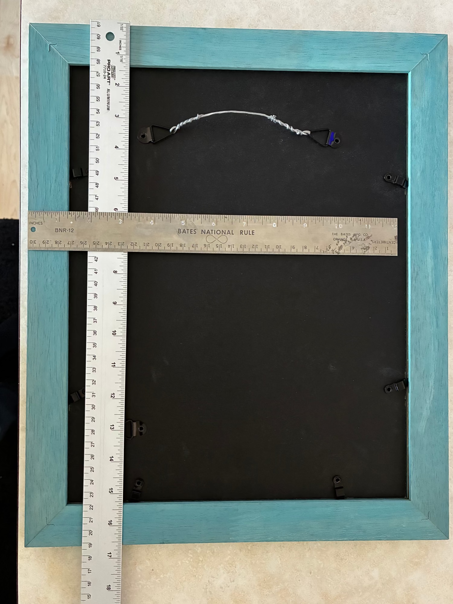 Back of a teal picture frame with a ruler for scale on a beige surface
