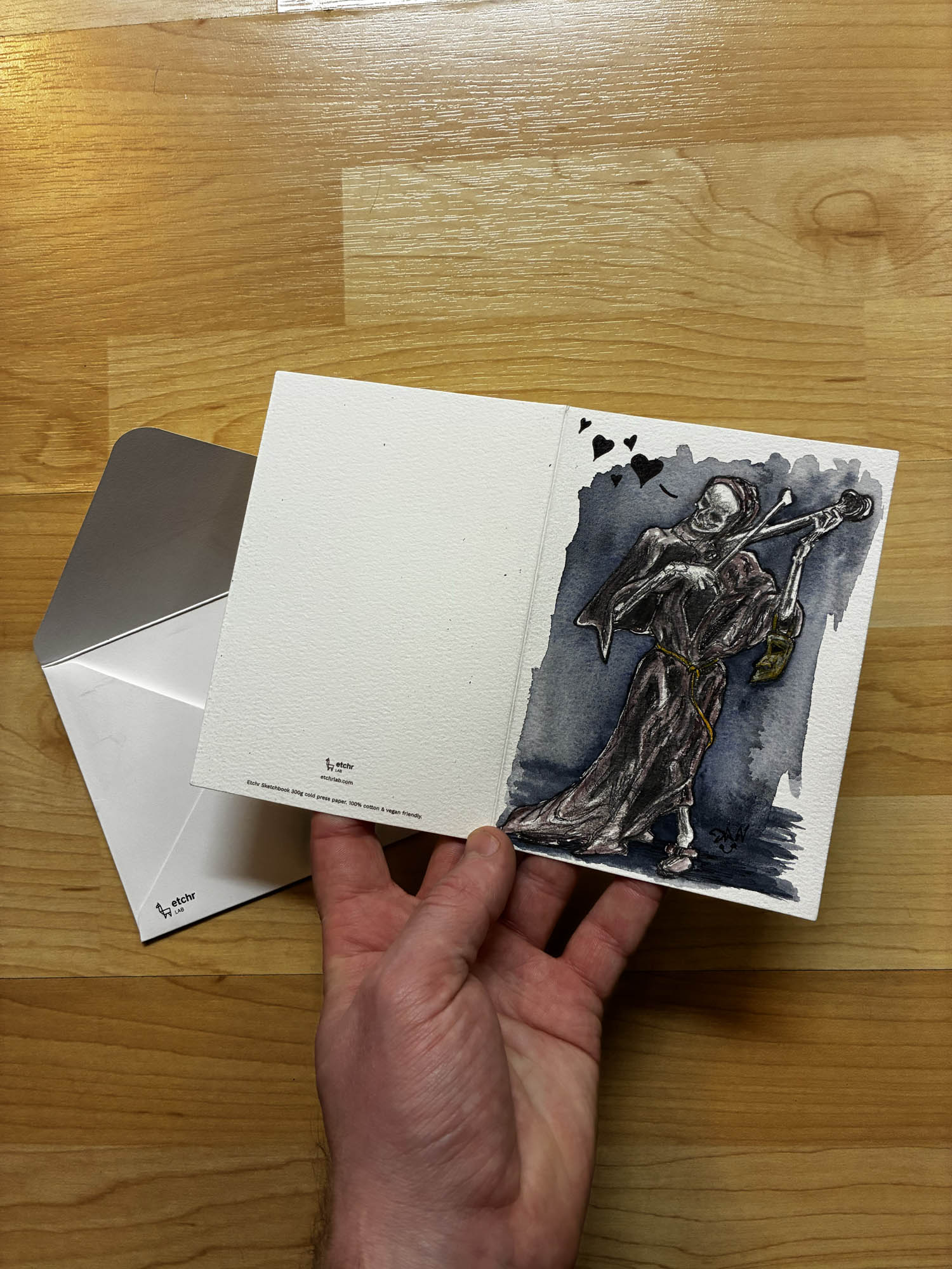 Hand holding a card with a skeleton playing guitar illustration on a wooden surface