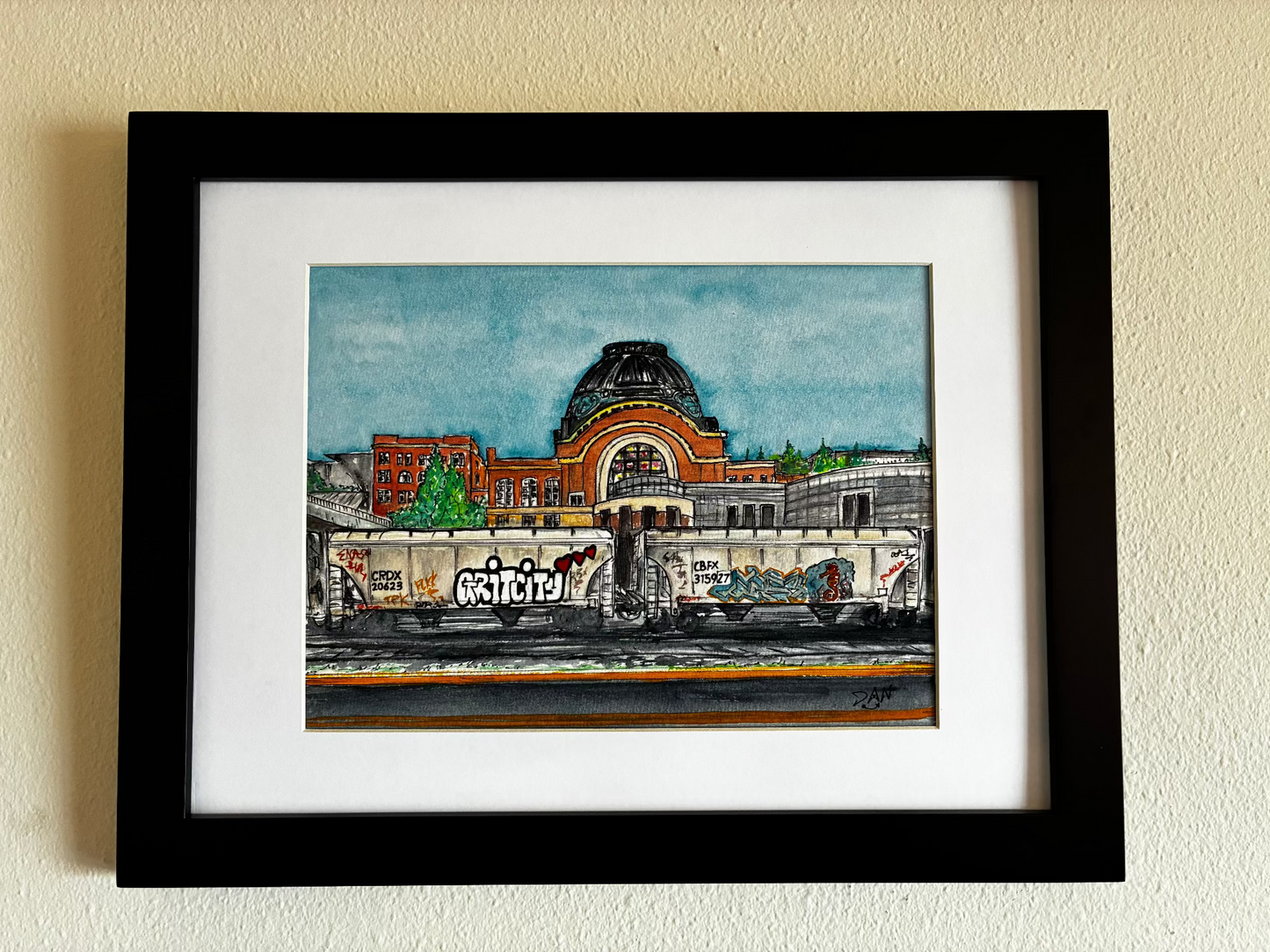 Framed artwork of a cityscape with a prominent building on a beige wall.