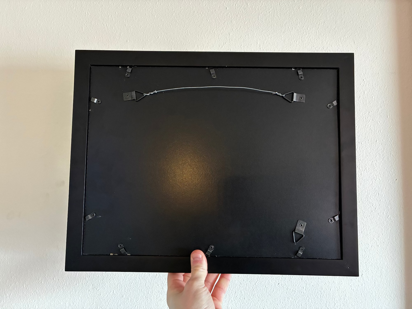 Black picture frame held against a white wall