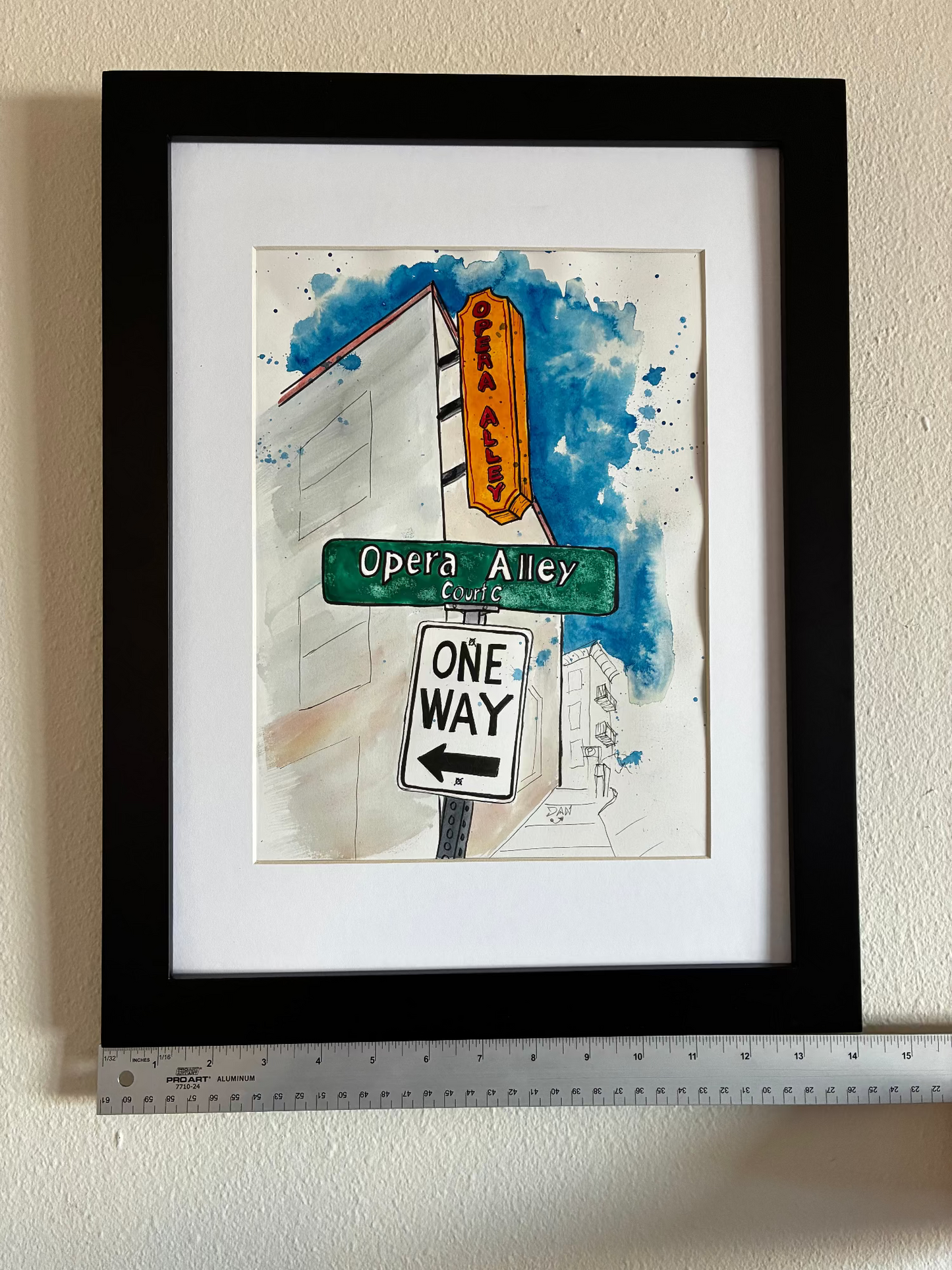 Framed artwork of street signs with a ruler for scale on a beige wall.