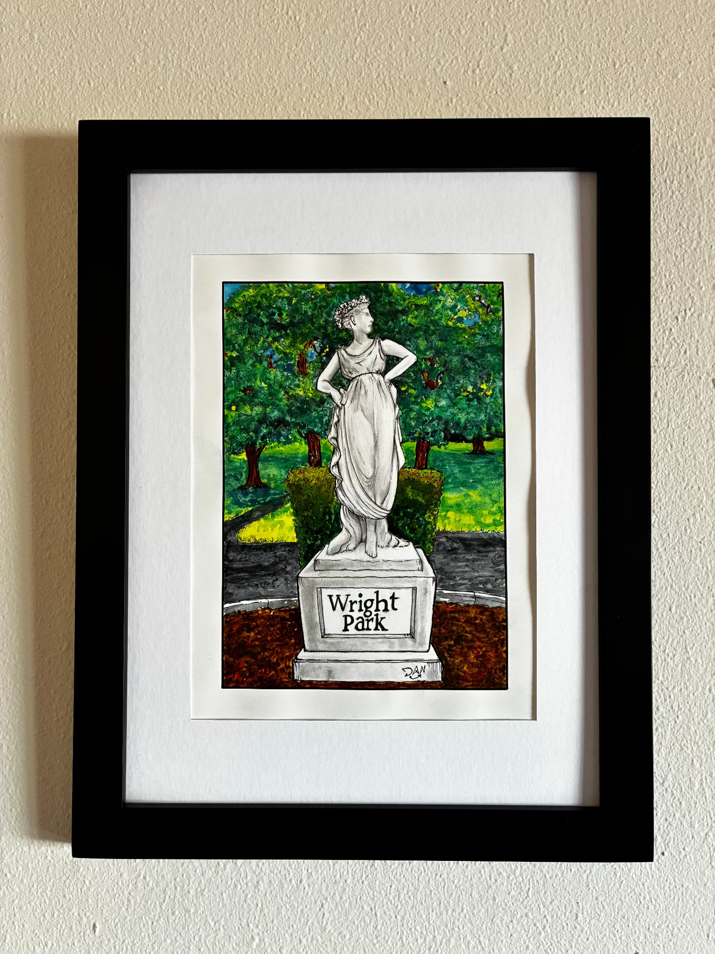 Framed artwork of a statue in a park setting on a beige wall