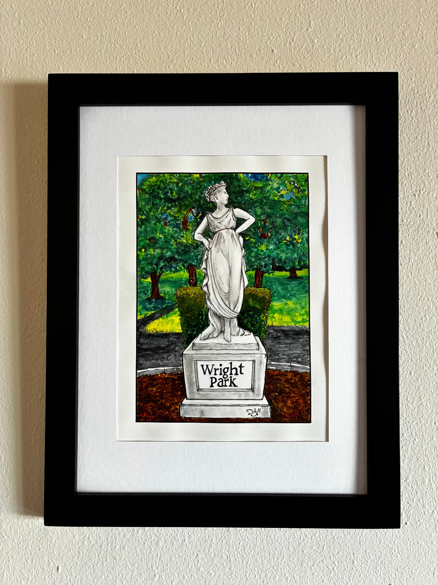 Framed artwork of a statue in a park setting on a beige wall