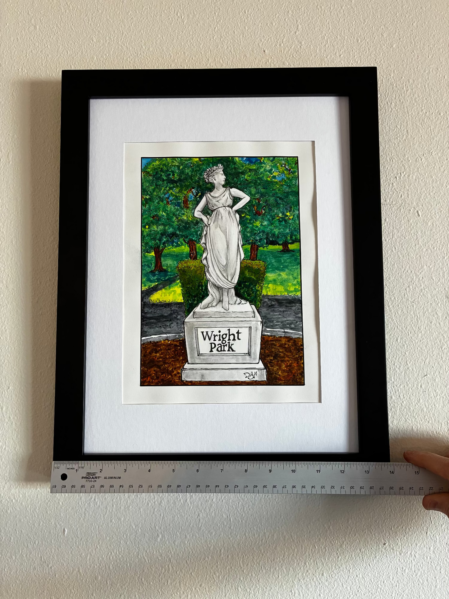 Framed artwork of a statue with 'Wright Park' text, held up against a wall with a ruler for scale.