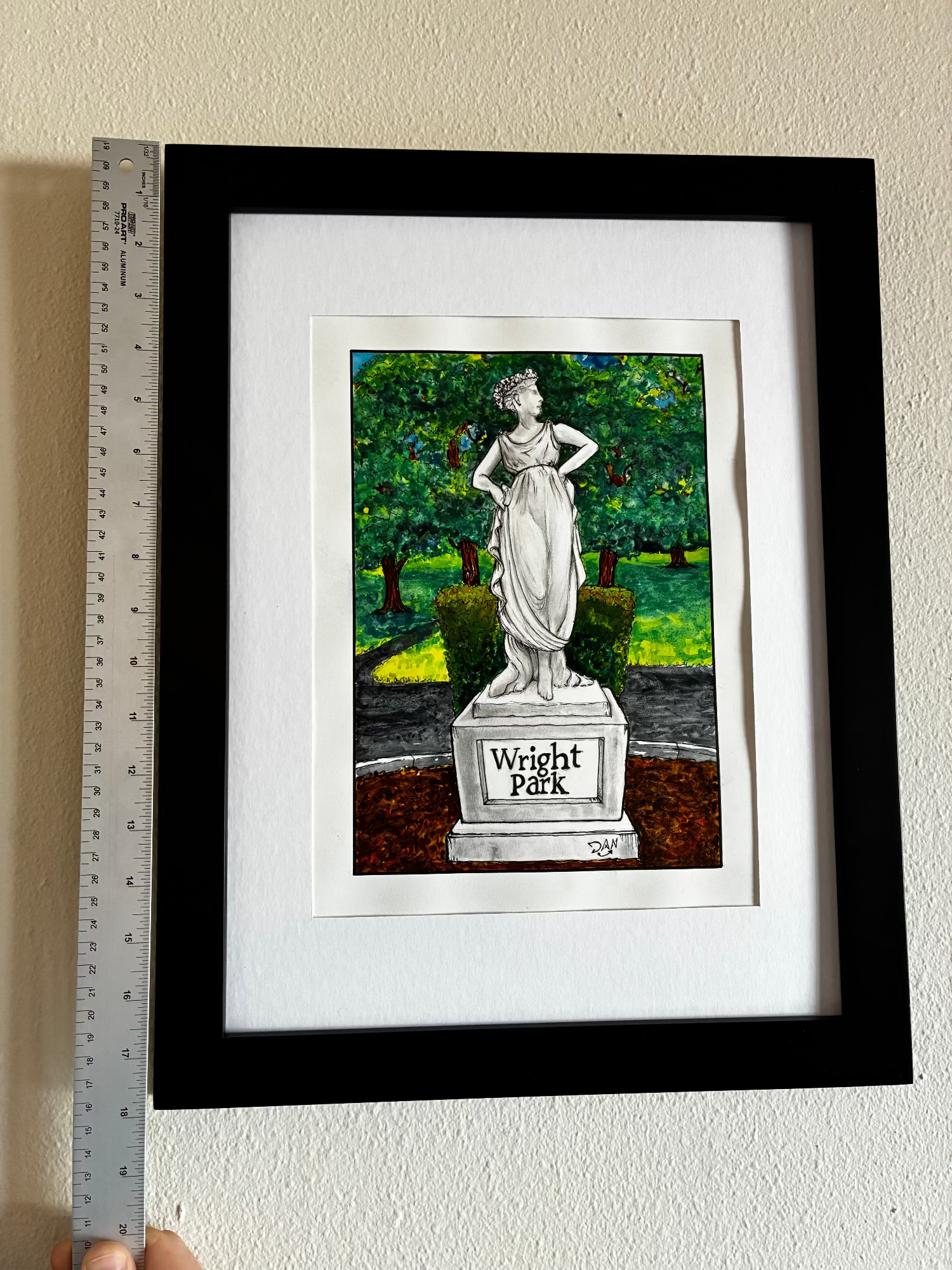Framed artwork of a statue with 'Wright Park' text, held up against a wall with a ruler for scale.