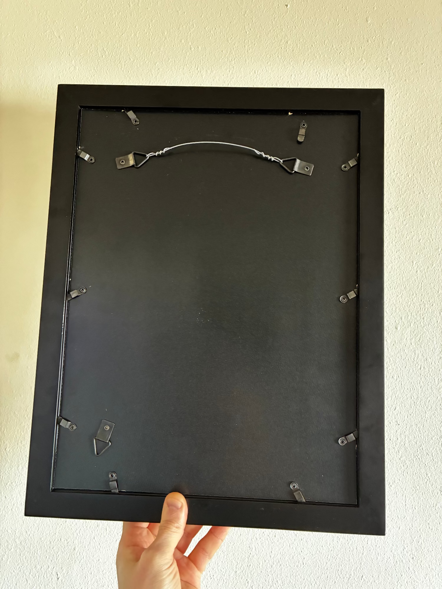 Black picture frame held against a white wall