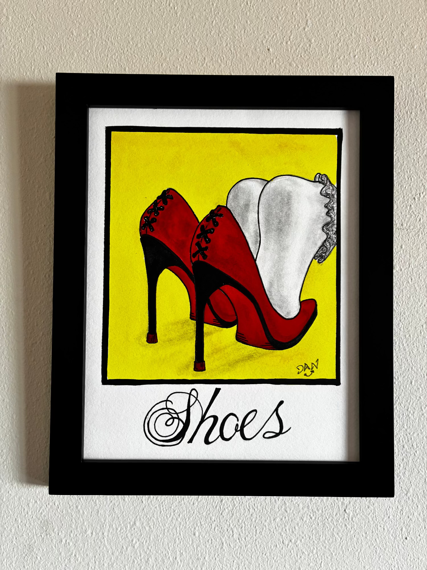 Framed artwork of red high-heeled shoes and white stockings on a yellow background.