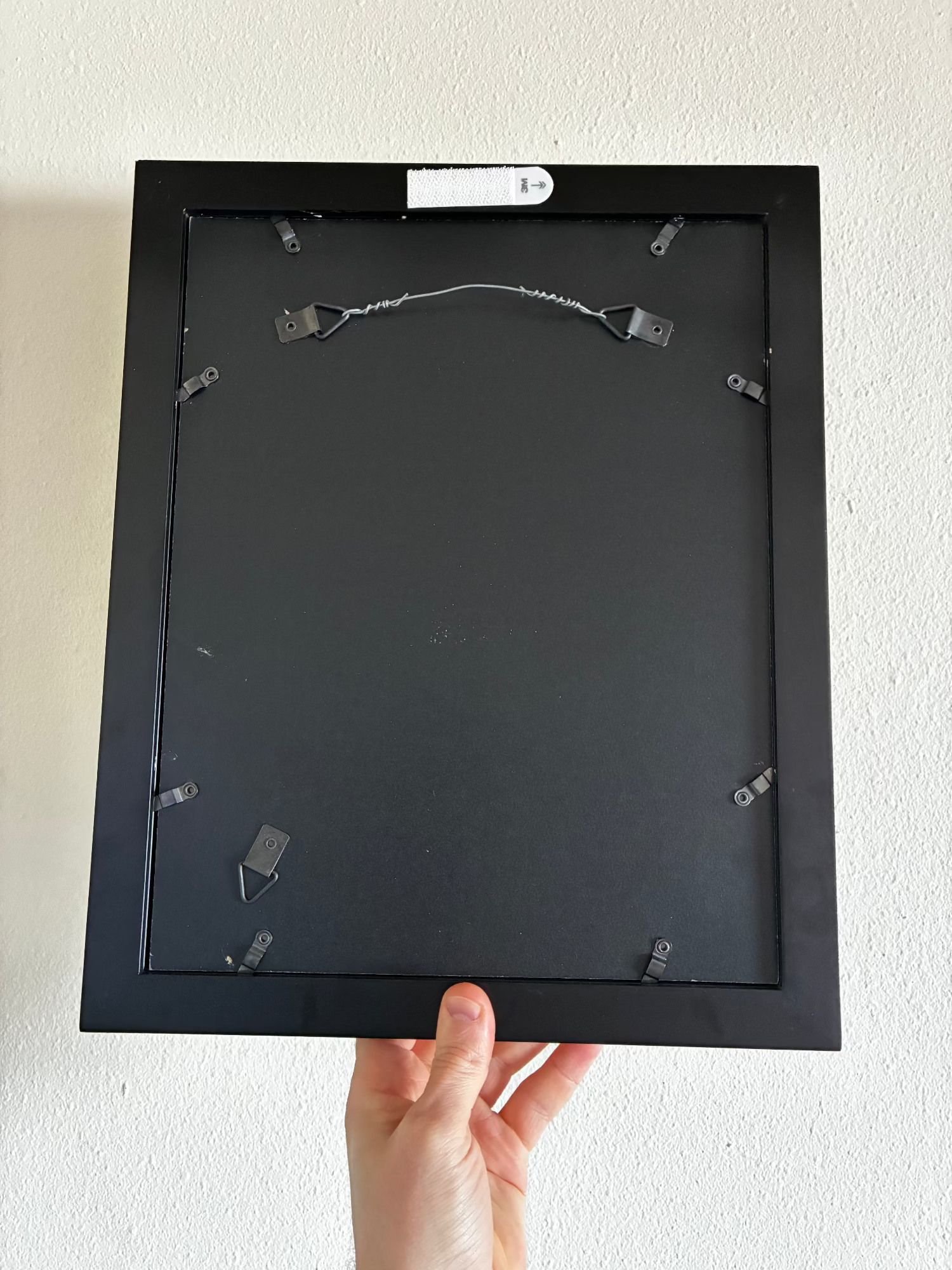 Black picture frame held by a hand against a white wall