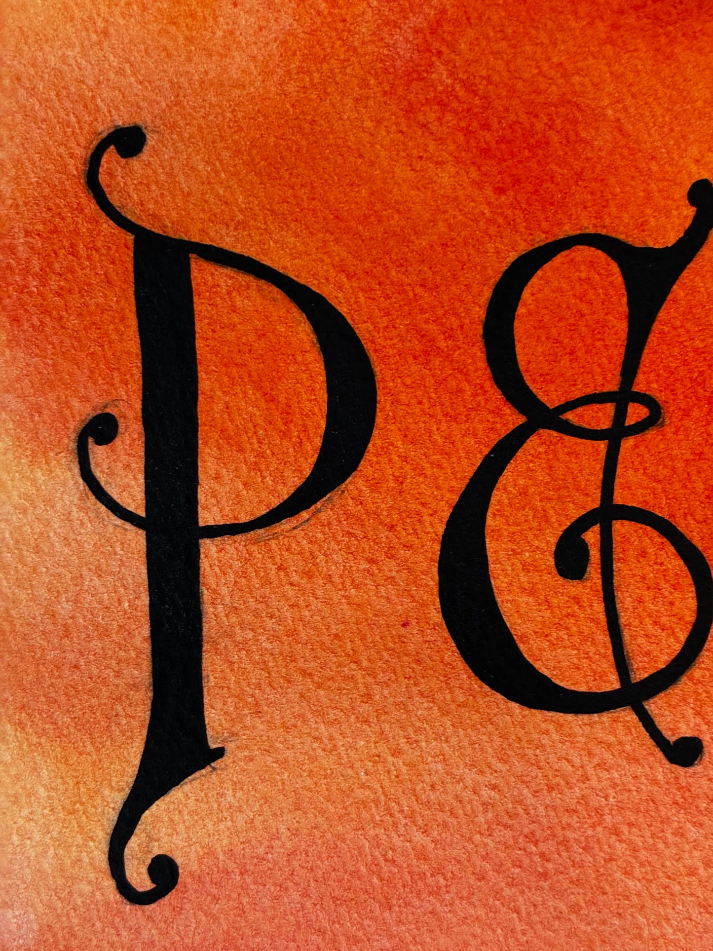 A close-up of a black decorative serif letter P and ampersand & on a warm orange watercolor background.