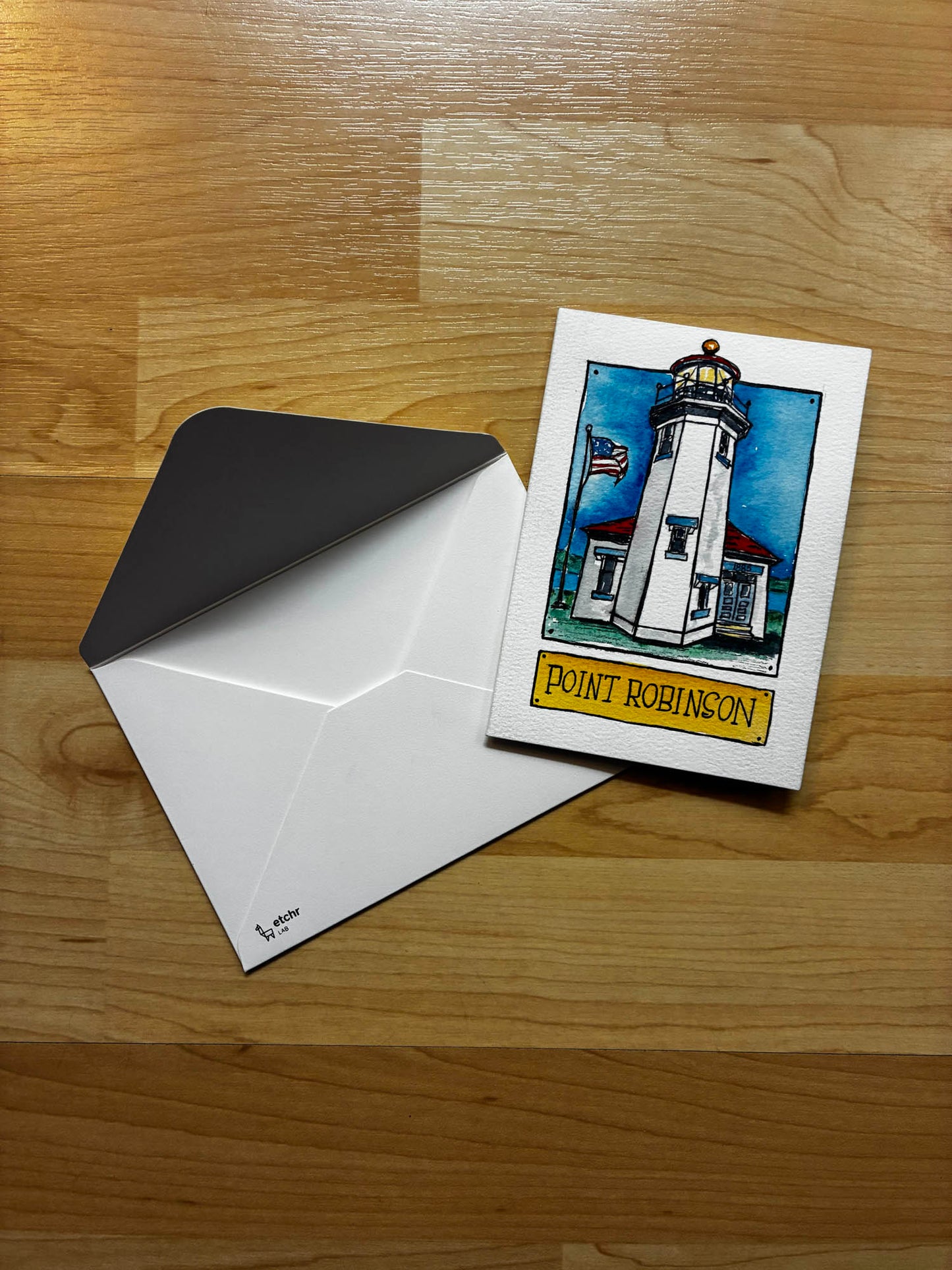 Greeting card with lighthouse illustration and envelope on a wooden surface