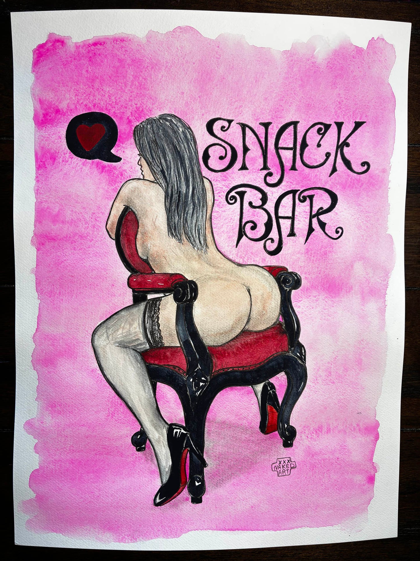 A watercolor art print depicting a nude woman with long dark hair sitting on a red and black chair, viewed from behind, with a speech bubble containing a red heart and the text 'SNACK BAR' in black script. The print is shown on a white sheet of paper against a dark wooden background.