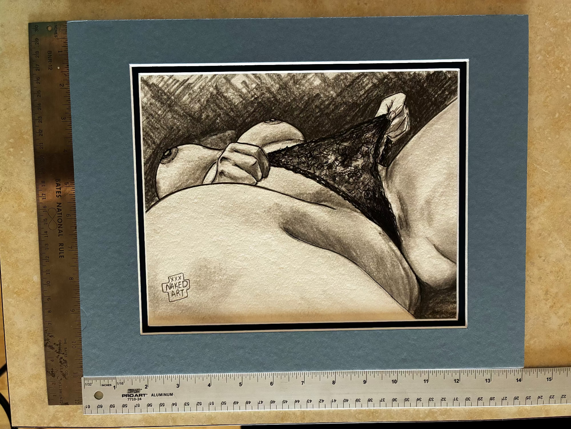 Matted and framed black and white drawing of a nude figure with a hand on a textured surface.