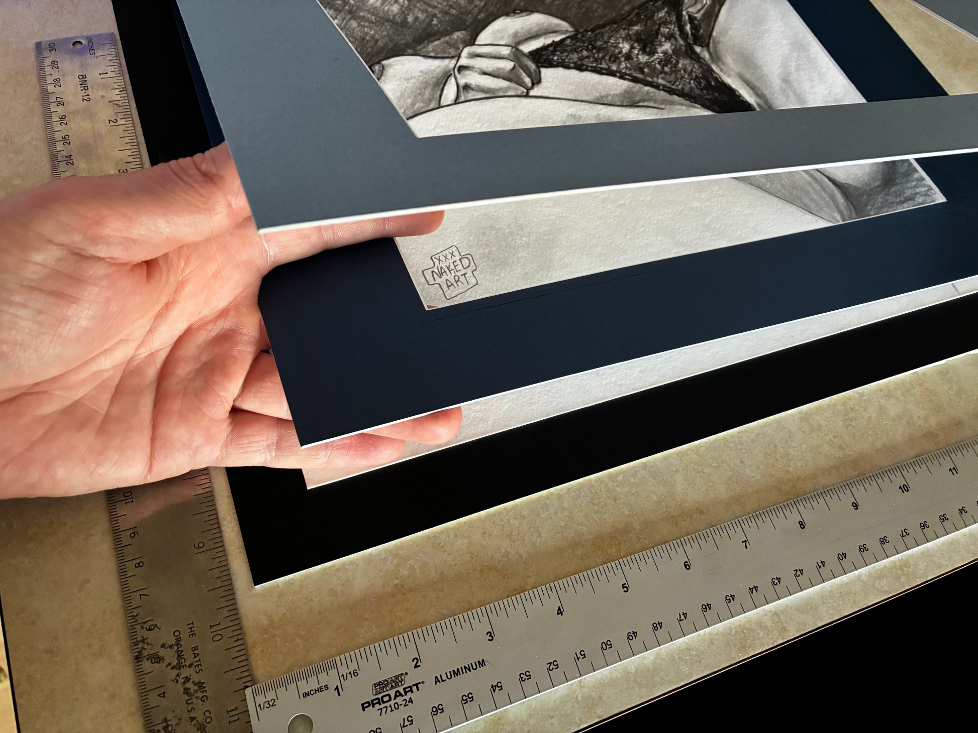 Hand adjusting a black mat behind a framed black and white photograph with a ruler for measurement.